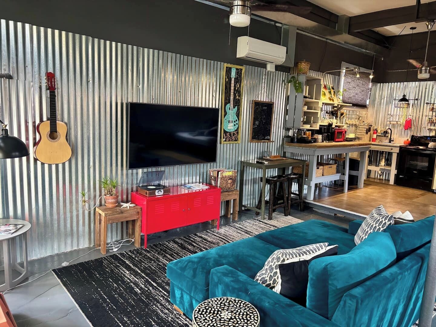 Una sala de estar moderna con un televisor grande, un mueble de entretenimiento rojo y un sofá color turquesa.