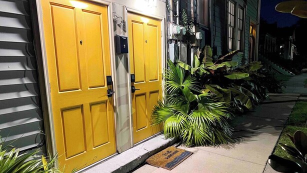 A building with two yellow doors, a small awning, and a doormat with text. - Chic Algiers Point loft with king bed. Walk to ferry, minutes to French Quarter & jazz. (New Orleans)