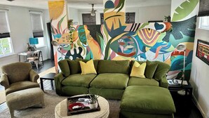 A modern living room with a sectional sofa, a round ottoman, and abstract wall art. - Chic Algiers Point loft with king bed. Walk to ferry, minutes to French Quarter & jazz. (New Orleans)