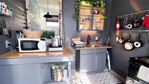 A compact kitchen with a microwave, toaster, and small sink. There is a shelf with kitchen utensils and a hanging pot rack. - Chic Algiers Point loft with king bed. Walk to ferry, minutes to French Quarter & jazz. (New Orleans)