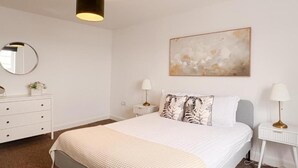 Una camera da letto con un letto, una cassettiera, un comodino, una lampada, uno specchio e un quadro appeso al muro.