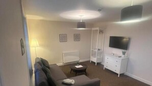 A living room with a sofa, a coffee table, a TV, and a white dresser. - Church View Apartment - Nelson's Retreat (Great Yarmouth)
