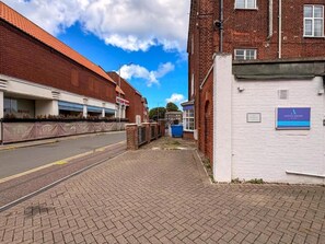 Gadescene med en murstensbygning, en lukket butik med et skodder, og et skilt, der angiver 'ASTON SHAW Customer Parking'.