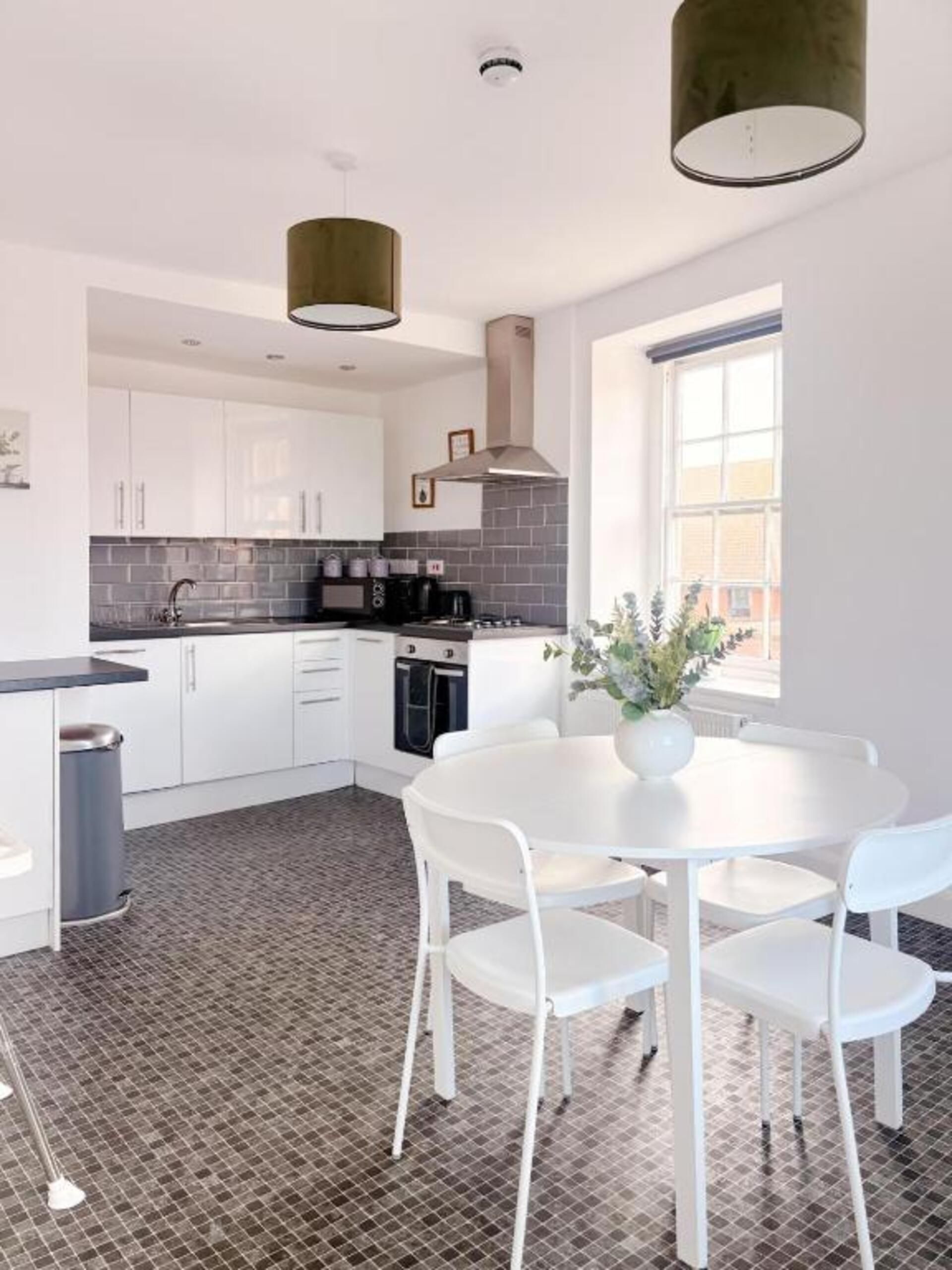 A modern kitchen with white cabinets, a black tiled backsplash, and a round white table with chairs.