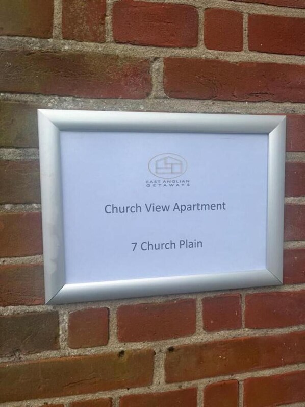 A sign for Church View Apartment at 7 Church Plain, framed in a silver border, mounted on a brick wall. - Church View Apartment - Nelson's Retreat (Great Yarmouth)