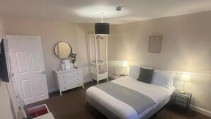 A bedroom with a bed, bedside tables, a wardrobe, a mirror, and a door. - Church View Apartment - Nelson's Retreat (Great Yarmouth)