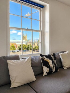 Una habitación con un ventanal grande, un sofá gris y vistas a un edificio histórico.