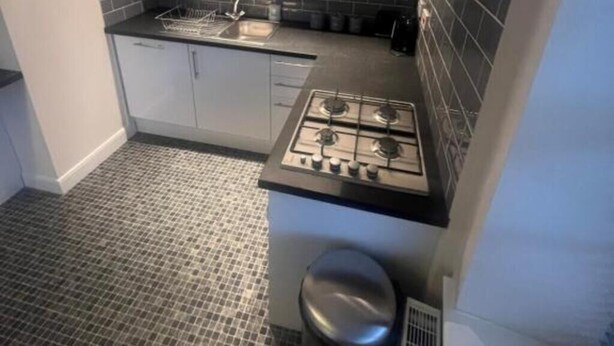 A compact kitchen with a gas stove, white cabinets, and a black tiled backsplash. - Church View Apartment - Nelson's Retreat (Great Yarmouth)