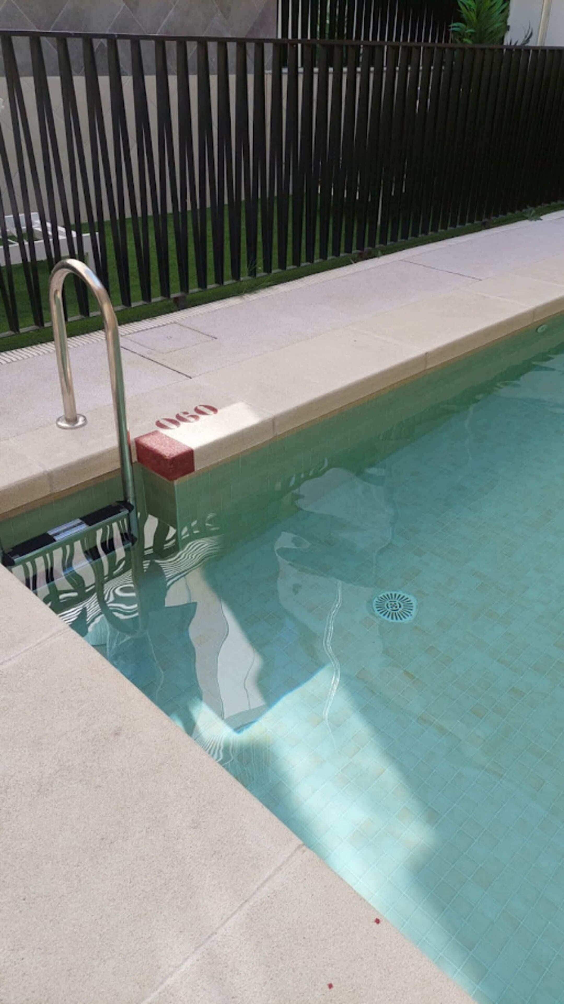 Ein Schwimmbecken mit einer Metallleiter und einer gefliesten Kante.