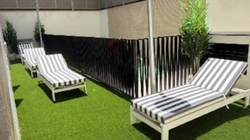 Eine Terrassenfläche mit drei Liegestühlen und einem kleinen grünen Rasen.