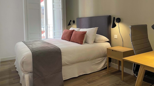 A bedroom with a bed, bedside table, chair, and a view of the outside.
