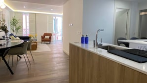 A modern kitchen with a central island, a dining area with a round table, and a living room with a sofa and armchair.