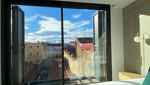 Une chambre avec une grande fenêtre, un lit et une table de chevet.