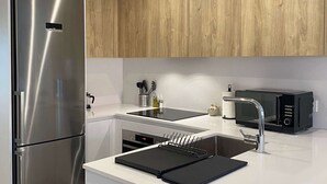 Une cuisine moderne dotée d’un réfrigérateur en acier inoxydable, d’un four à micro-ondes noir et d’un plan de travail blanc.