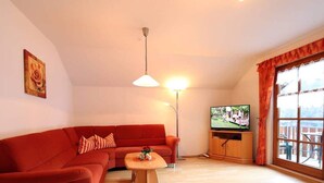 Ein Wohnzimmer mit einem roten Sofa, einem Holztisch, einem Fernseher auf einem Holzschrank und einem großen Fenster mit Vorhängen.