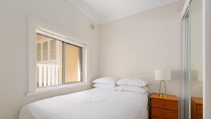 A bedroom with a bed, a window, a nightstand, and a mirror. - Chic 1-bed Retreat Near Shops & Beach (Sydney)
