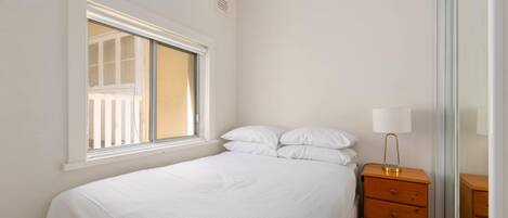 Un dormitorio con cama, ventana, mesita de noche y espejo.