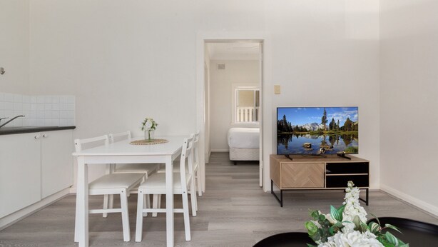 A modern living room with a dining area, a TV on a wooden stand, and a view of a lake through the window. - Chic 1-bed Retreat Near Shops & Beach (Sydney)