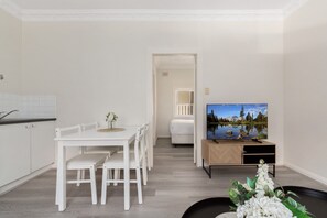 A modern living room with a dining area, a TV on a wooden stand, and a view of a lake through the window. - Chic 1-bed Retreat Near Shops & Beach (Sydney)