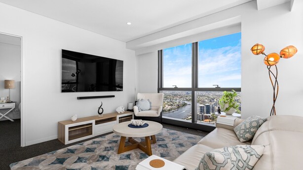 A modern living room with a large TV, comfortable seating, a coffee table, and a view of a cityscape through large windows.