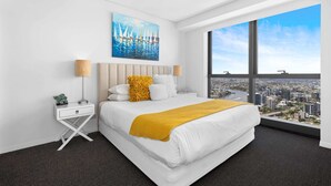A modern hotel room with a large bed, a city view, a painting on the wall, and a nightstand with a lamp.