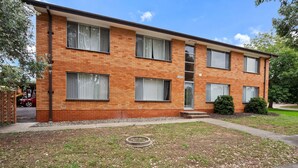 A two-story brick apartment building with a flat roof, large windows, and a small front yard with a lawn and a tree. - Comfortable 1-bed Retreat Near Canberra City (Canberra)