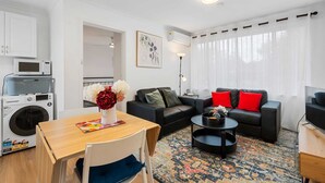 A modern living room with a sofa, coffee table, and a dining area with a table and chairs. - Comfortable 1-bed Retreat Near Canberra City (Canberra)