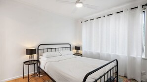 A bedroom with a bed, two bedside tables with lamps, a ceiling fan, and a window with curtains. - Comfortable 1-bed Retreat Near Canberra City (Canberra)