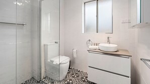 A modern bathroom with a glass-enclosed shower, a toilet, a sink with a mirror above it, and patterned floor tiles. - Comfortable 1-bed Retreat Near Canberra City (Canberra)
