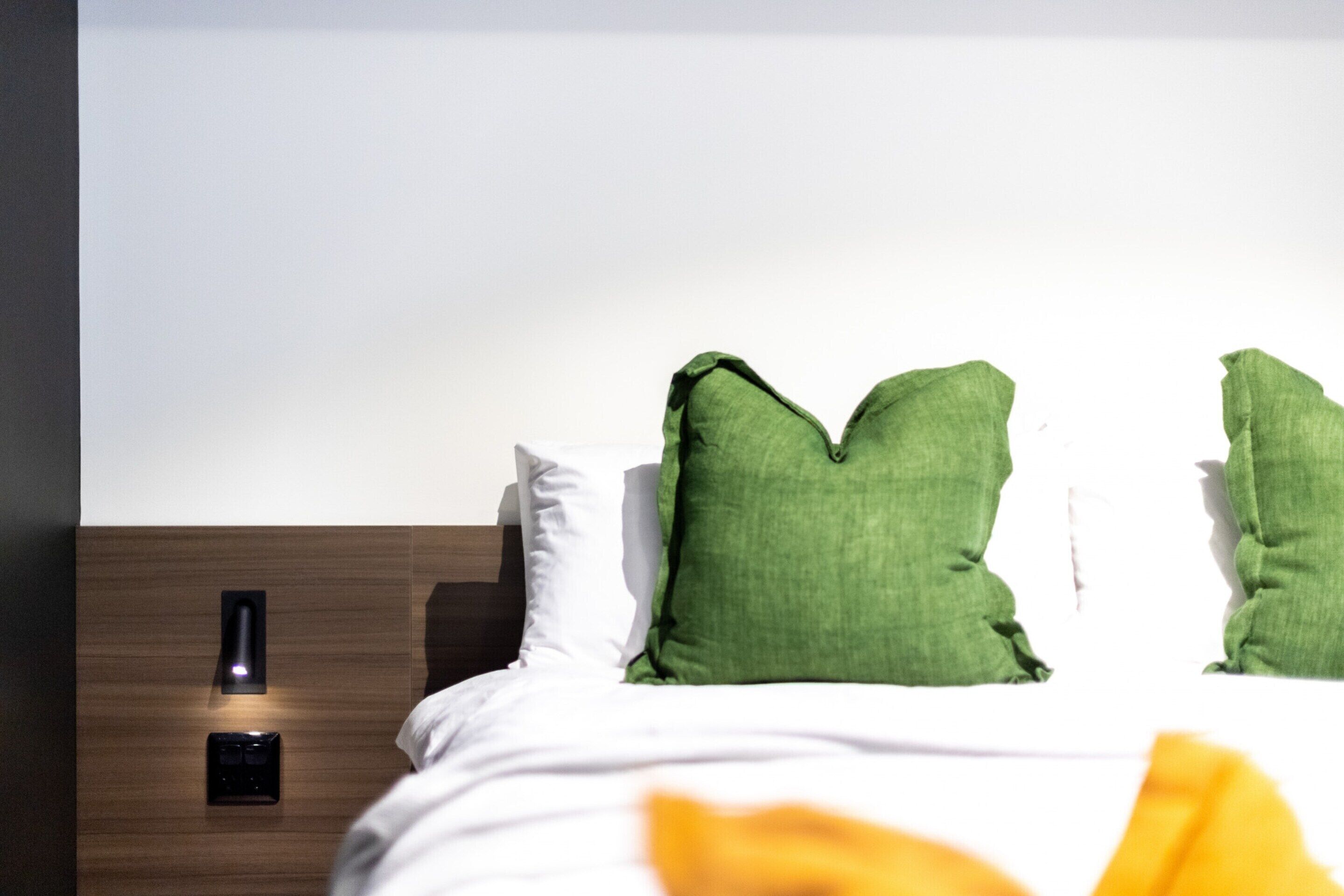 Ein Hotelzimmer mit einem hölzernen Kopfende, einer weißen Bettdecke und grünen Kissen.