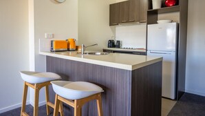 A compact kitchen with a central island, two bar stools, a refrigerator, and a clock on the wall. - Spacious City Stay Near Lygon Street Dining (Melbourne)
