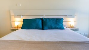 A neatly made bed with a white duvet and two teal pillows, flanked by bedside tables with lamps. - Spacious City Stay Near Lygon Street Dining (Melbourne)