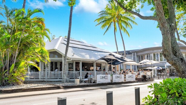 A beachfront restaurant with outdoor seating, palm trees, and umbrellas. - Beachfront 3-bed With Pool & Stunning Ocean Views (Cairns)