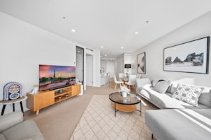 A modern living room with a flat-screen TV, a sofa, a coffee table, and a dining area. - Stylish 2-bed Apartment in Canberra CBD (Canberra)