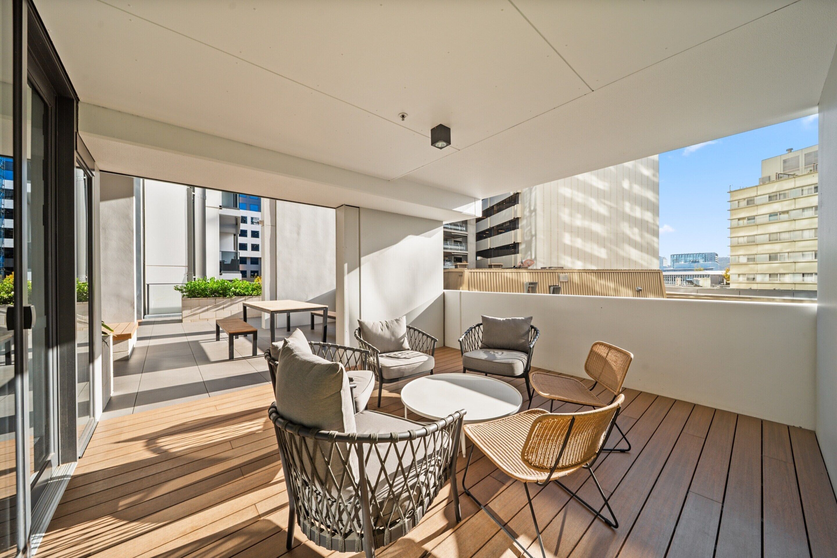 A modern outdoor balcony with wooden flooring, wicker furniture, and a view of the cityscape.