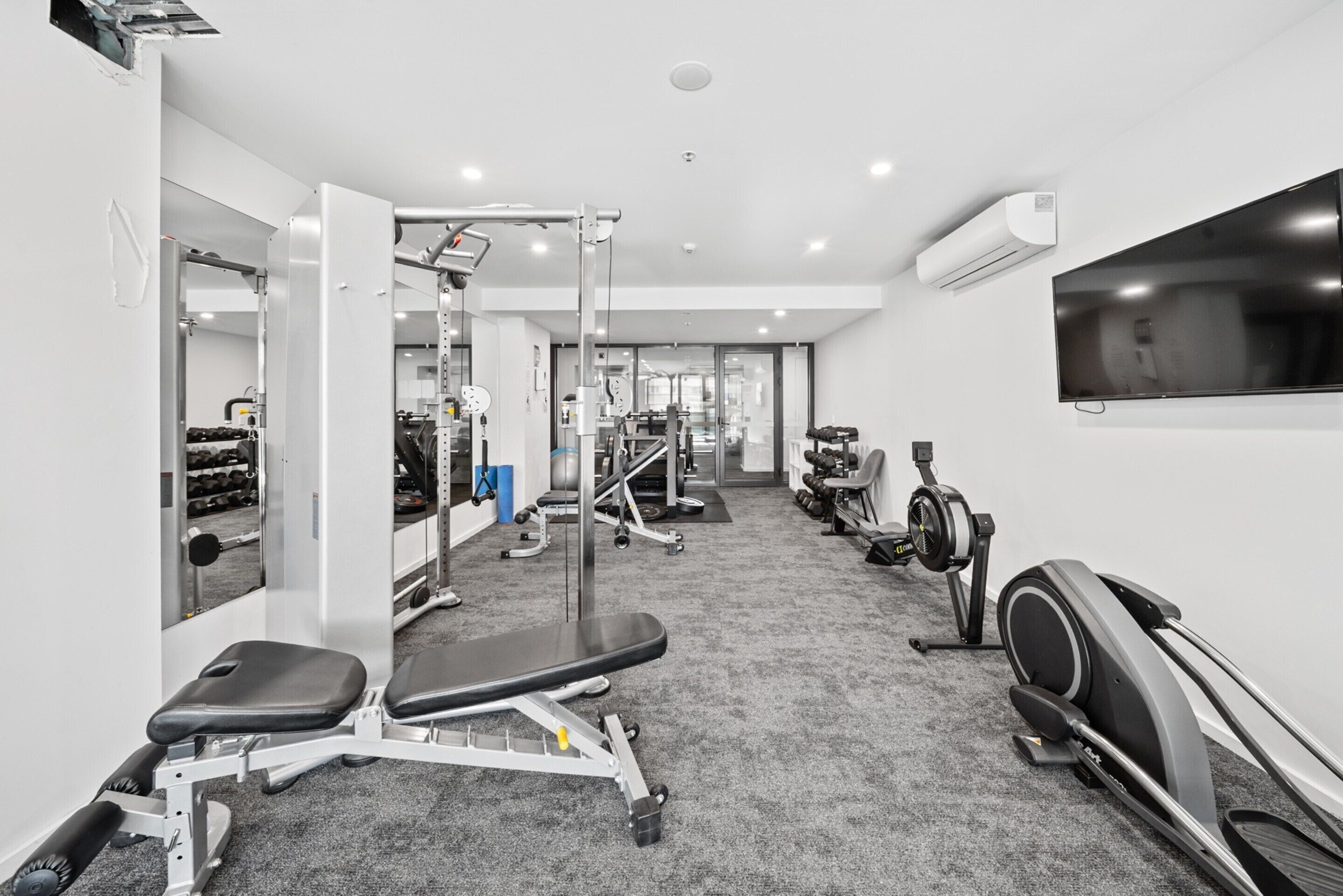A gym with cardio equipment, weight machines, and a TV on the wall.