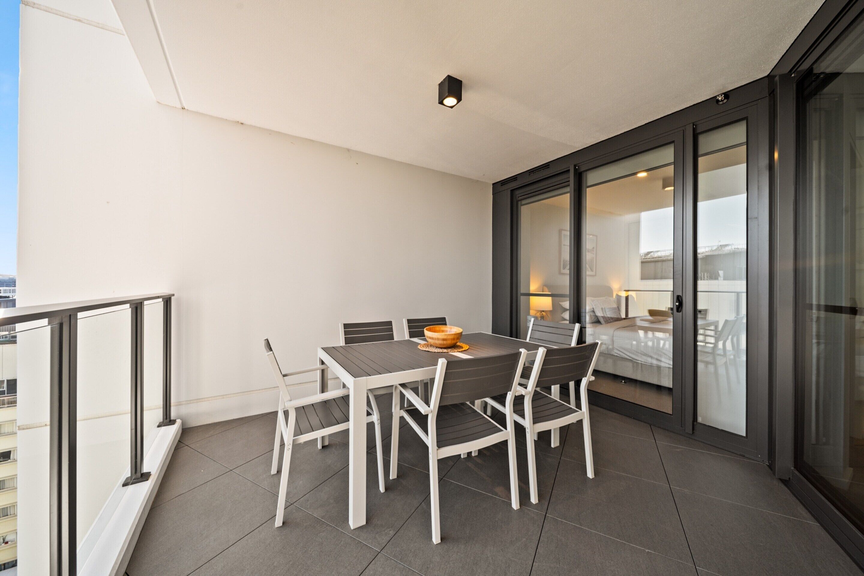 A balcony with a dining table and chairs, a sliding glass door leading to a bedroom, and a city view.