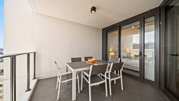 A balcony with a dining table and chairs, a sliding glass door leading to a bedroom, and a city view.