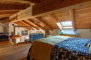 A bedroom with a wooden ceiling, a bed with a polka dot cover, a desk with a lamp, and a window.