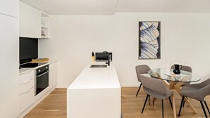 A modern kitchen with white cabinetry, a central island, and a dining area with a glass table and four chairs. - Idyllic 1-bed Near Popular Shopping Streets (Melbourne)
