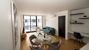 A modern living room with a glass dining table, grey chairs, a teal sofa, and a black door. - Idyllic 1-bed Near Popular Shopping Streets (Melbourne)