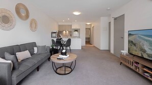 Un salon moderne avec un canapé gris, une table basse ronde et un téléviseur à écran plat posé sur un meuble en bois.