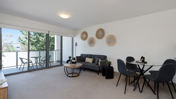 Un salon moderne avec un canapé, une table basse et une table à manger. Il y a de grandes fenêtres et un balcon.