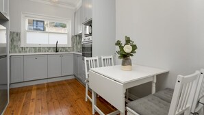 A kitchen with white cabinets, a white table, and a window. - Coastal Living Just Metres From Coogee Beach (Sydney)