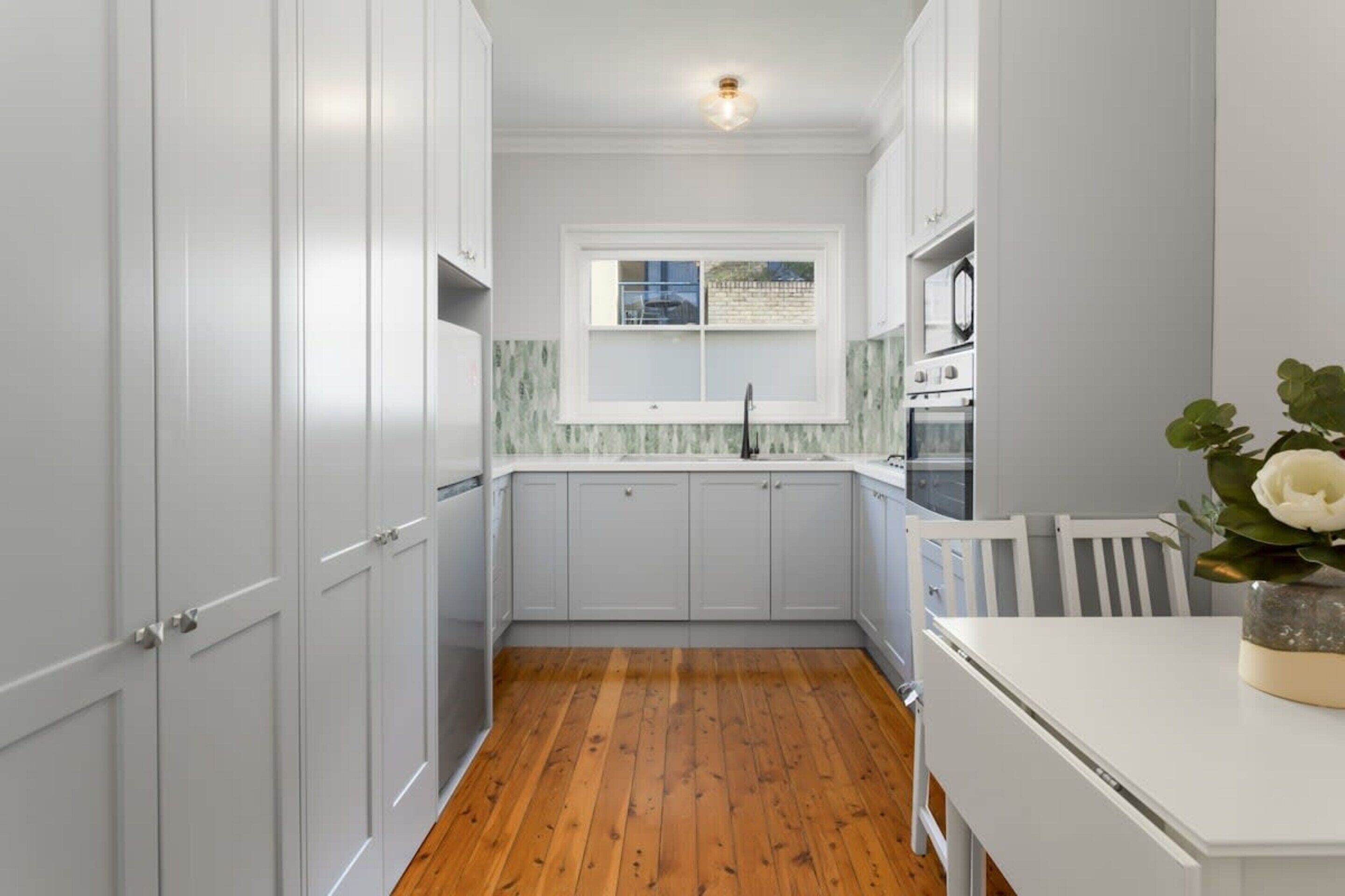 A kitchen with white cabinets, a wooden floor, and a window with a view.