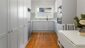 A kitchen with white cabinets, a wooden floor, and a window with a view. - Coastal Living Just Metres From Coogee Beach (Sydney)