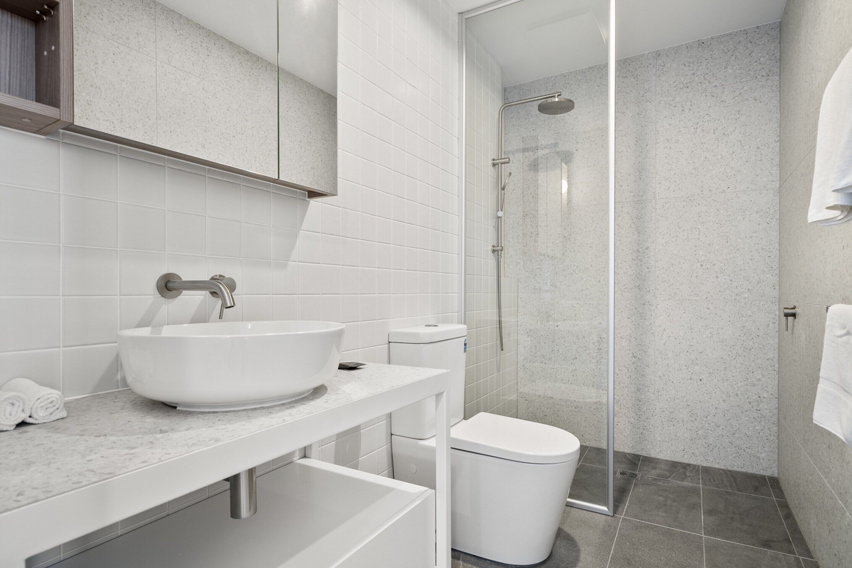 Une salle de bain moderne avec un lavabo, des toilettes et une douche, le tout de couleur blanche.