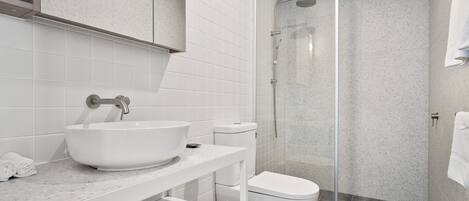 Une salle de bain moderne avec un lavabo, des toilettes et une douche, le tout de couleur blanche.