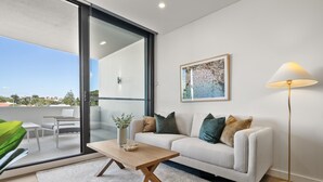 En moderne stue med sofa, sofabord og gulvlampe. Der er en skydedør, der fører ud til et udendørs område med et bord og stole.