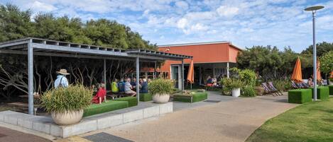 An outdoor seating area with a covered patio, potted plants, and a building in the background.